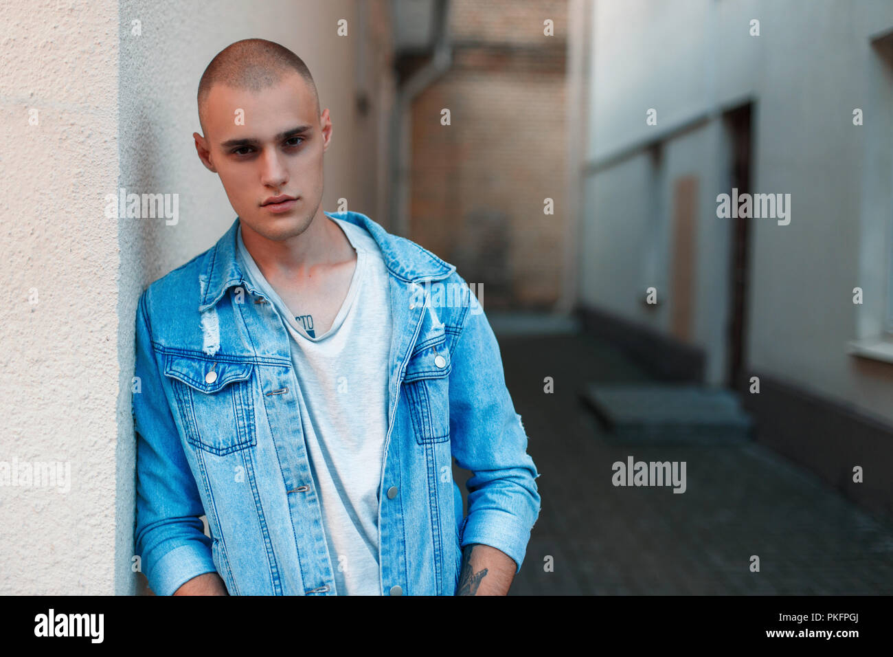Handsome stylish American man in a denim jacket and a gray T-shirt near a building on the street Stock Photo