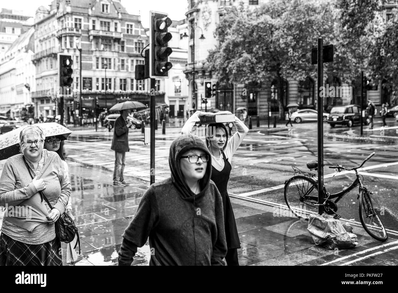 24 August 2018 - London, England. Black and white image of a group of people caught up in the bad weather. A woman covering with big old book from the Stock Photo