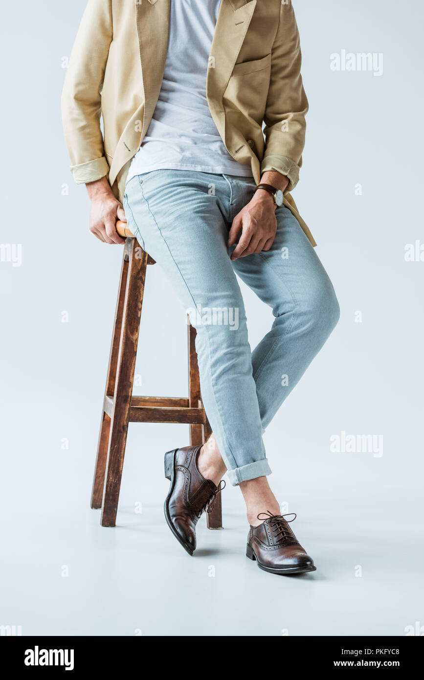Cropped view of stylish young man sitting on stool on white background Stock Photo