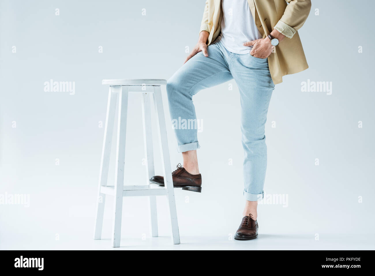 Cropped view of stylish young man leaning on stool on white background Stock Photo