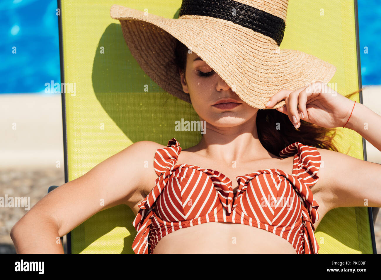 close-up portrait of attractive young woman in straw hat and bikini relaxing on sun lounger at poolside Stock Photo