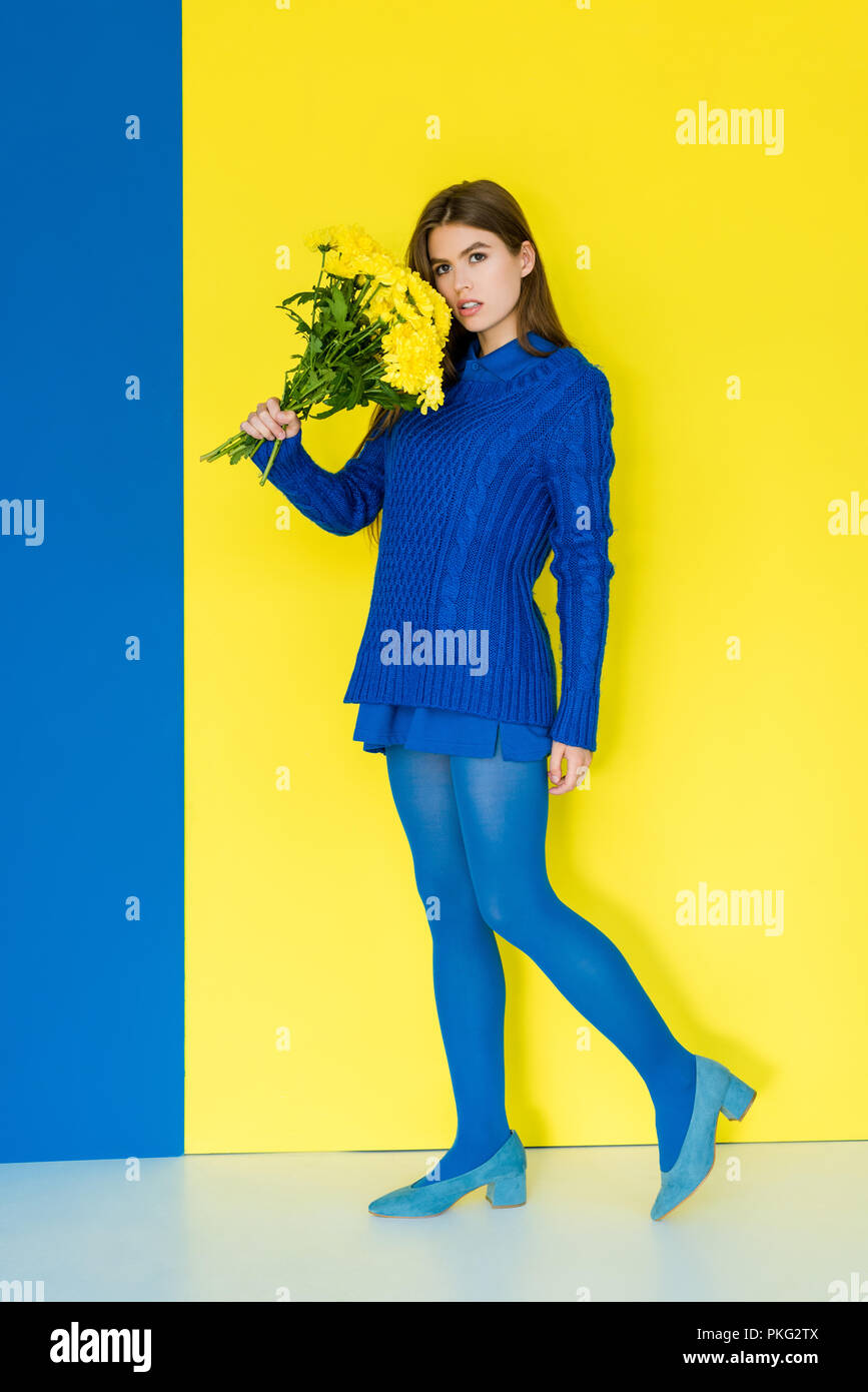 Attractive young girl in blue outfit holding yellow flowers on blue and ...