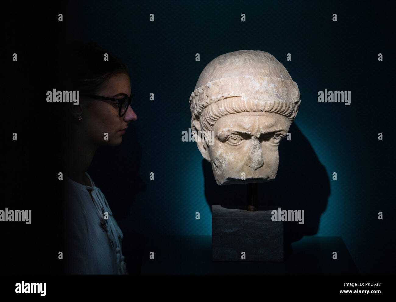 13 September 2018, Rhineland-Palatinate, Speyer: A museum staff member looks at the original portrait head of a Roman emperor, presumably Valentinian I. in the exhibition. The head is on loan from the Ny Carlsberg Glyptotek Museum in Copenhagen. In an exhibition entitled "Valentinian I and the Palatinate in Late Antiquity" (16 September 2018 to 11 August 2019), the Historical Museum of the Palatinate shows the work of the Roman Emperor Valentinian I during his period of office from 364 to 375 AD in the present Palatinate. Photo: Andreas Arnold/dpa Stock Photo