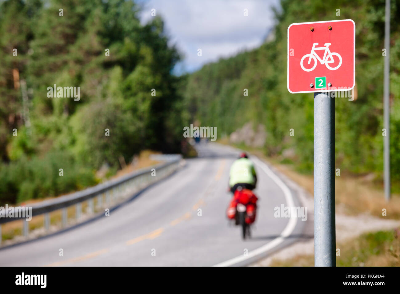 Road sign on a cycle route number 2 (The canal route) with traveling cyclist in background, Southern Norway Stock Photo