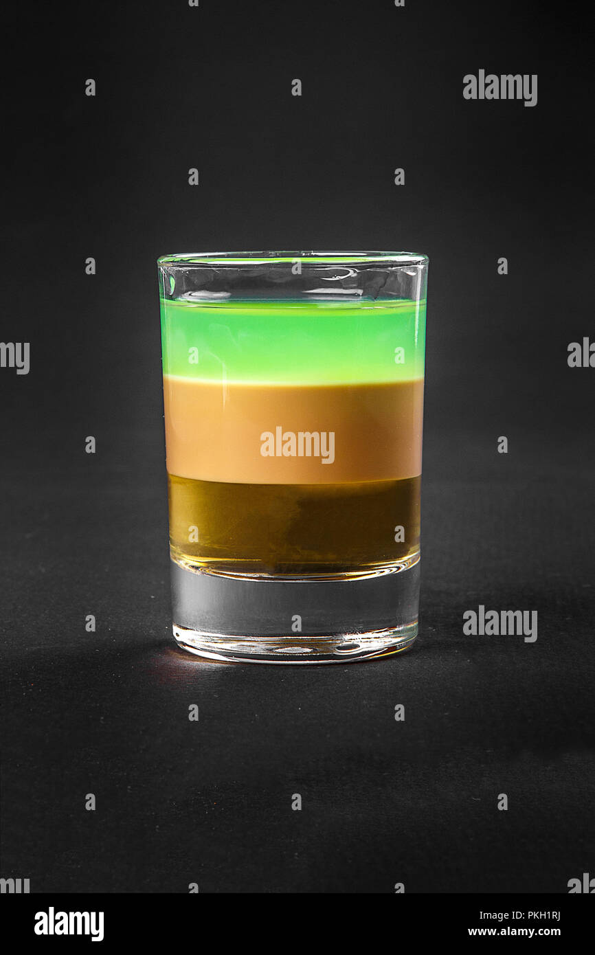 Multicolored layered cocktail, glass with transparent and colored drink with the taste of mint, banana, lemon, coffee, cream, absinthe, alcoholic, sid Stock Photo
