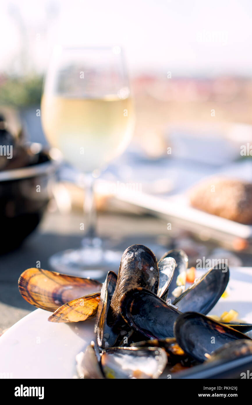 Mussels in a saucepan and a glass of cold white wine. Delicious seafood dinner in a restaurant on the beach. Copy space. Stock Photo