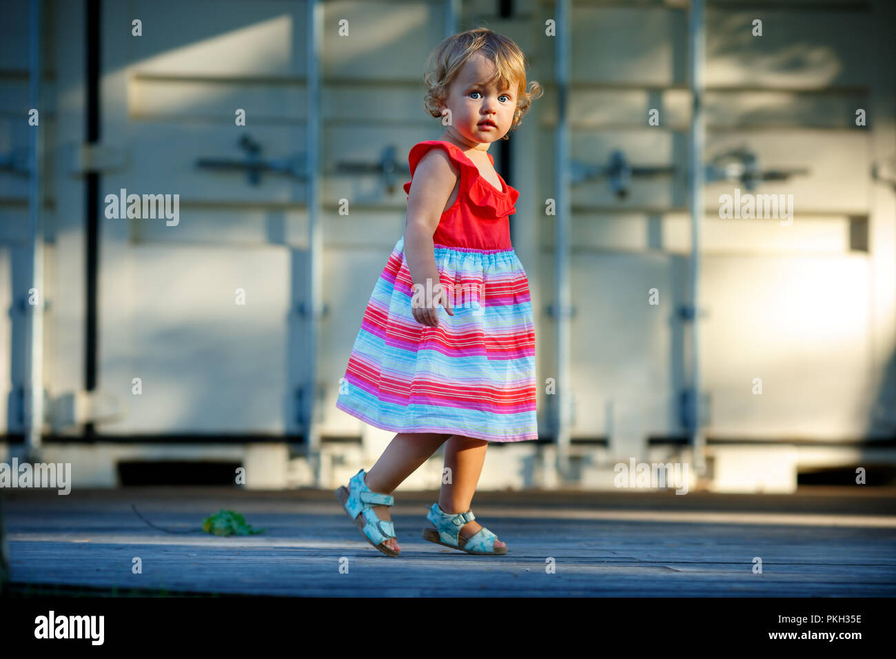 Sweet blond little baby girl in beautiful dress plays walks outdoors Stock Photo