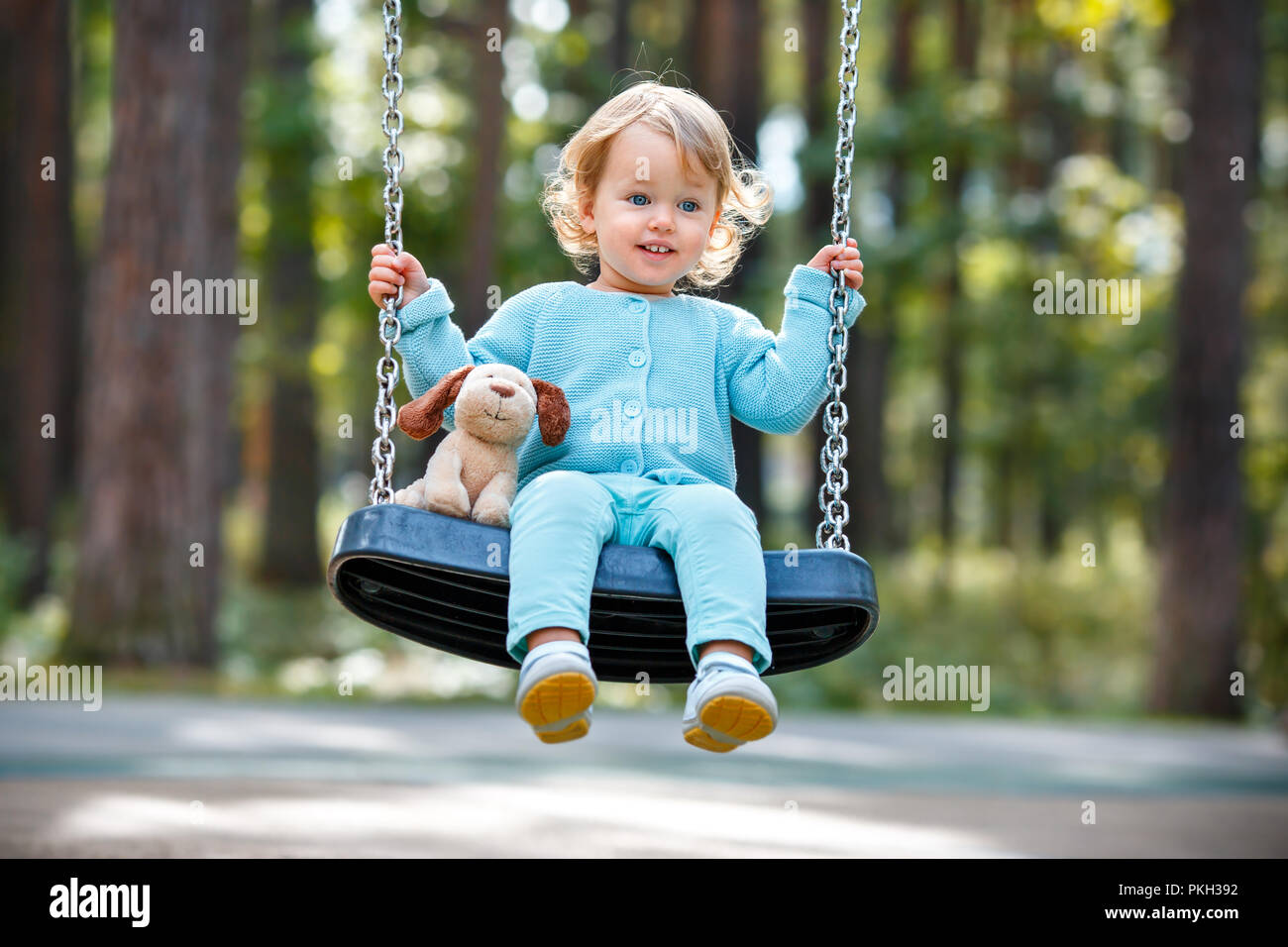 Adorable toddler girl with soft toy dog having fun on a swing on summer day Stock Photo