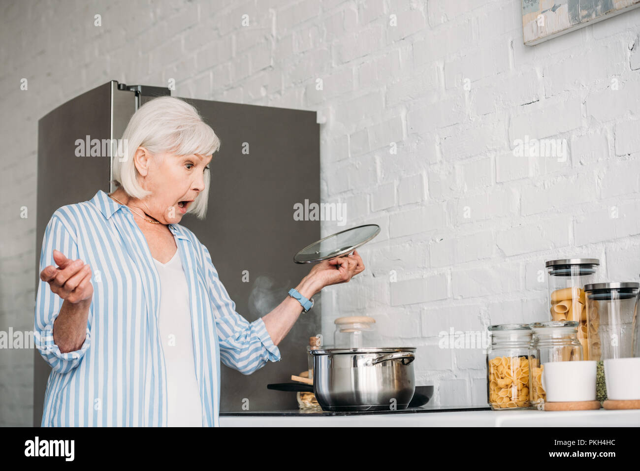 side view of shocked senior lady checking saucepan on stove in kitchen Stock Photo