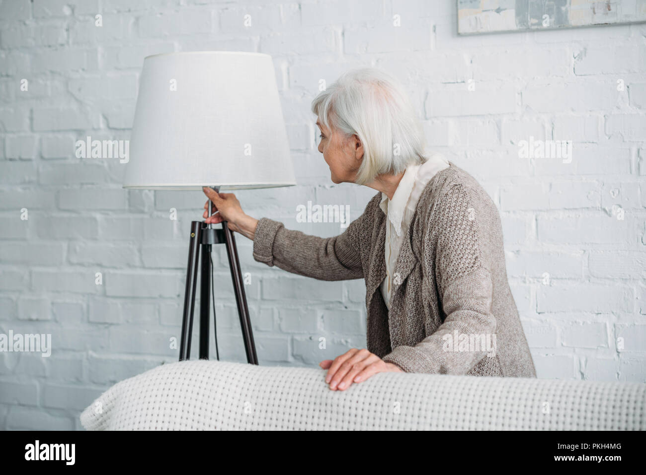 grey hair lady turning on standing lamp at home Stock Photo