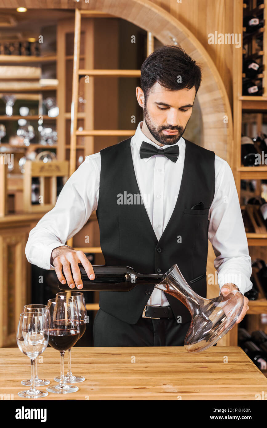 handsome young wine steward pouring wine into decanter at wine store