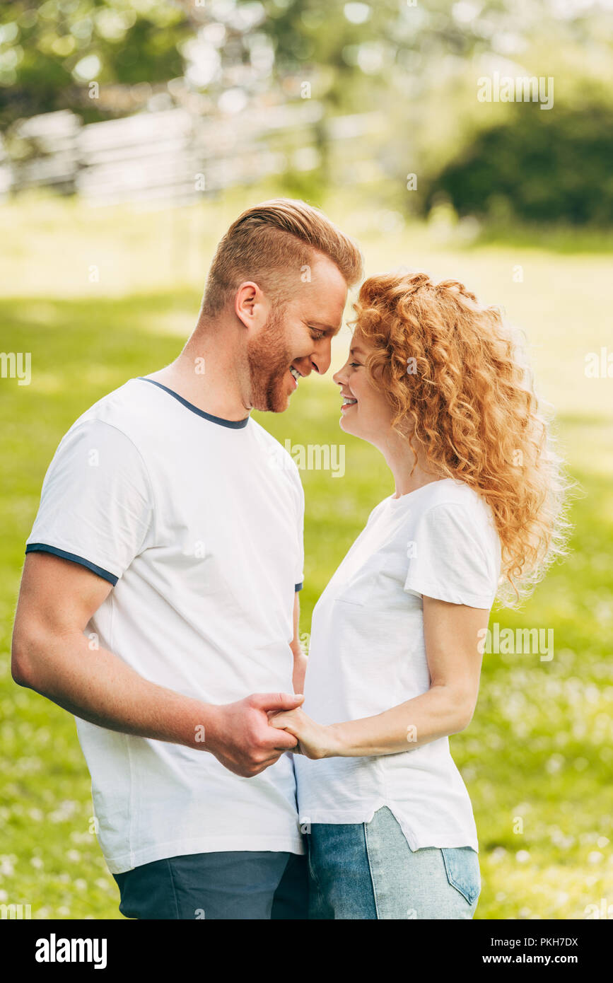 side view of happy young couple holding hands and smiling each other at ...