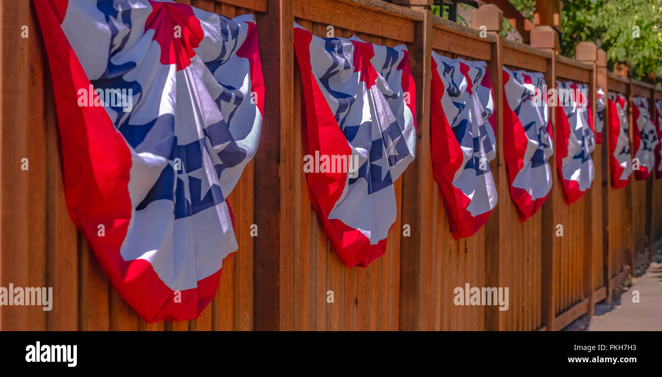 Patriotic flags hung on a wooden fence by sidewalk Stock Photo