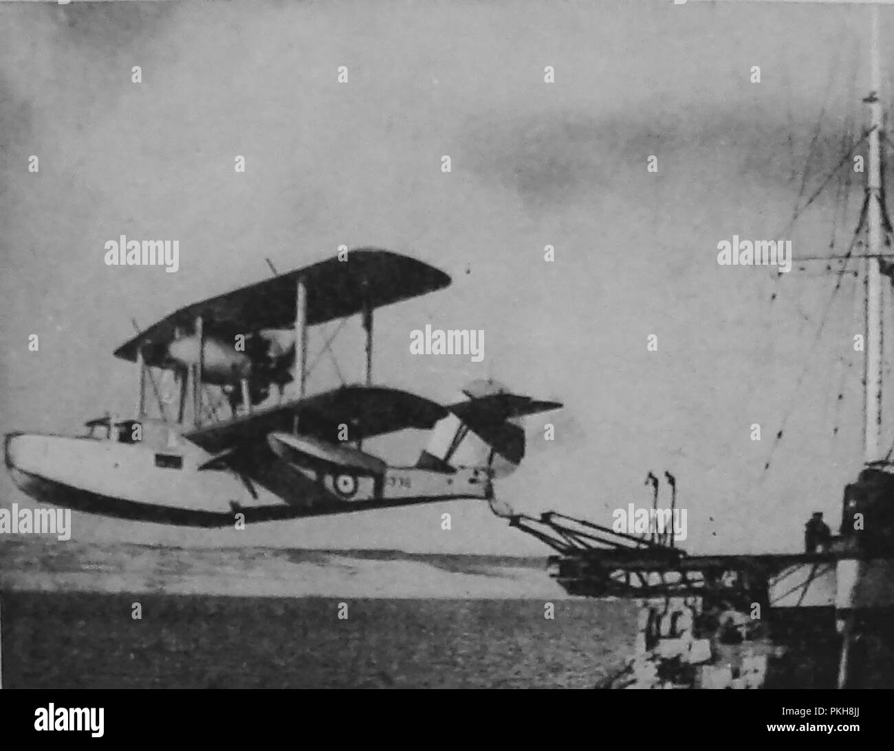 An old printed photograph showing an experimental aircraft carrier using a British biplane  (Seaplane) launched from a warship in 1933 Stock Photo