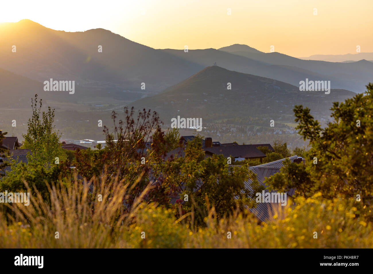 Sunset on mountains behind homes and trees Stock Photo
