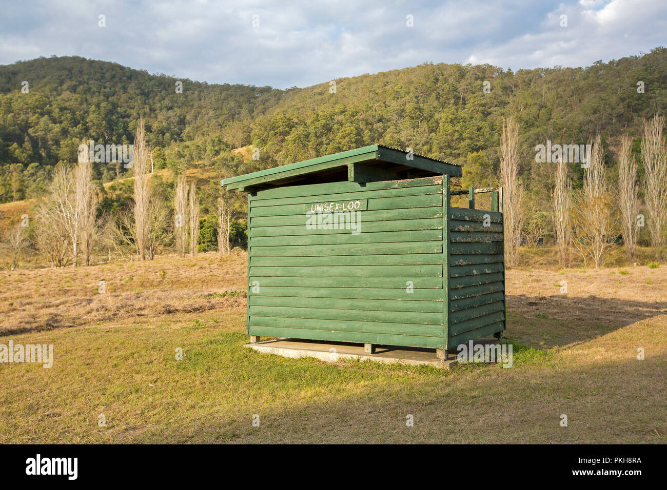 Wooden building housing pit toilet in field adjacent to forested hills at rural camping area in NSW Australia NSW Stock Photo