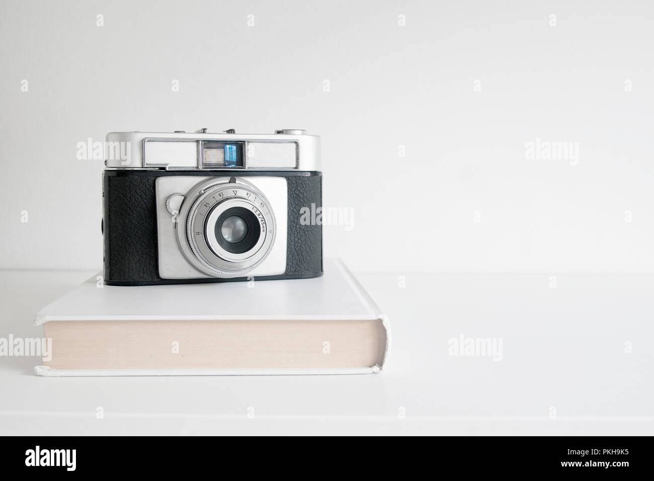 Camera on a white photo book on a wooden shelf. White background and empty copy space for Editor's text. Stock Photo