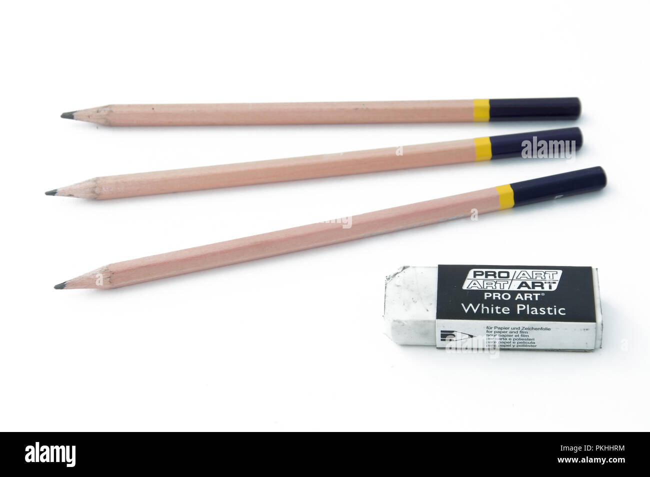 Three drawing pencils beside an rubber eraser and charcoal sticks on a white background. Stock Photo