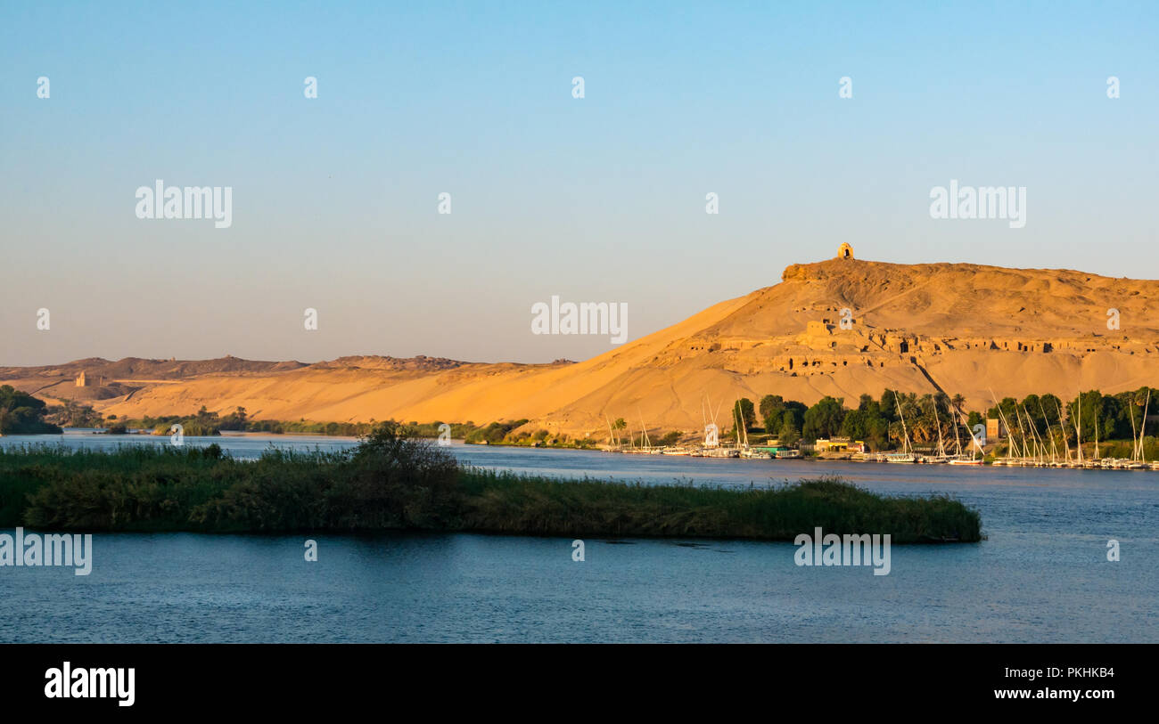 Aga Khan mausoleum and hilltop Qubbet el-Hawa tomb in early morning light with traditional felucca sailing boats, Nile River, Aswan, Egypt, Africa Stock Photo