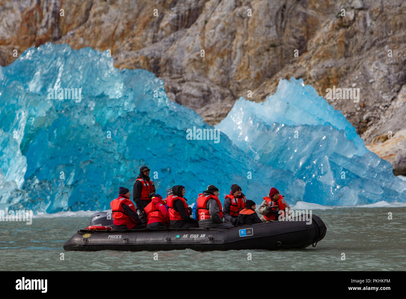 Ecotourists from Lindblad Expeditions enjoy cruising in a DIB and looking at a  blue iceberg in front of Dawe's glacier in Southeast Alaska Stock Photo