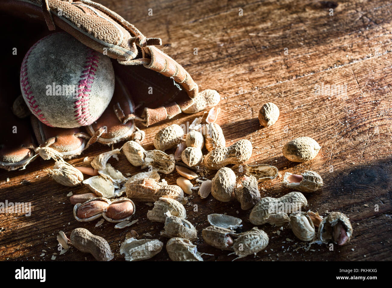 Old baseball glove and ball with peanuts in the shell on a background of rustic wood. Nostalgia concept or theme. Close up, texture detail Stock Photo