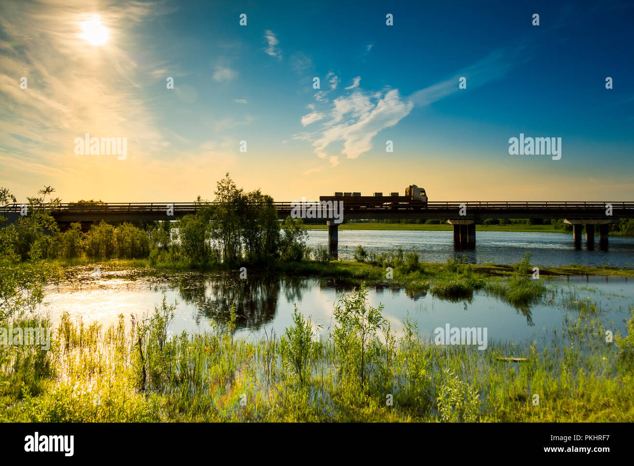 Sunrise over the bridge on which a truck is passing by against a flooded river Stock Photo