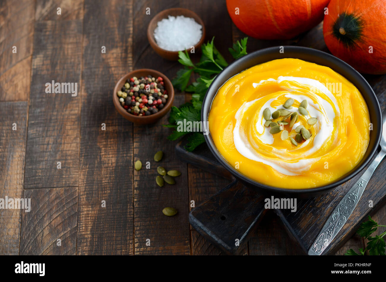 Pumpkin cream soup with cream and pumpkin seeds on rustic wooden table. Stock Photo