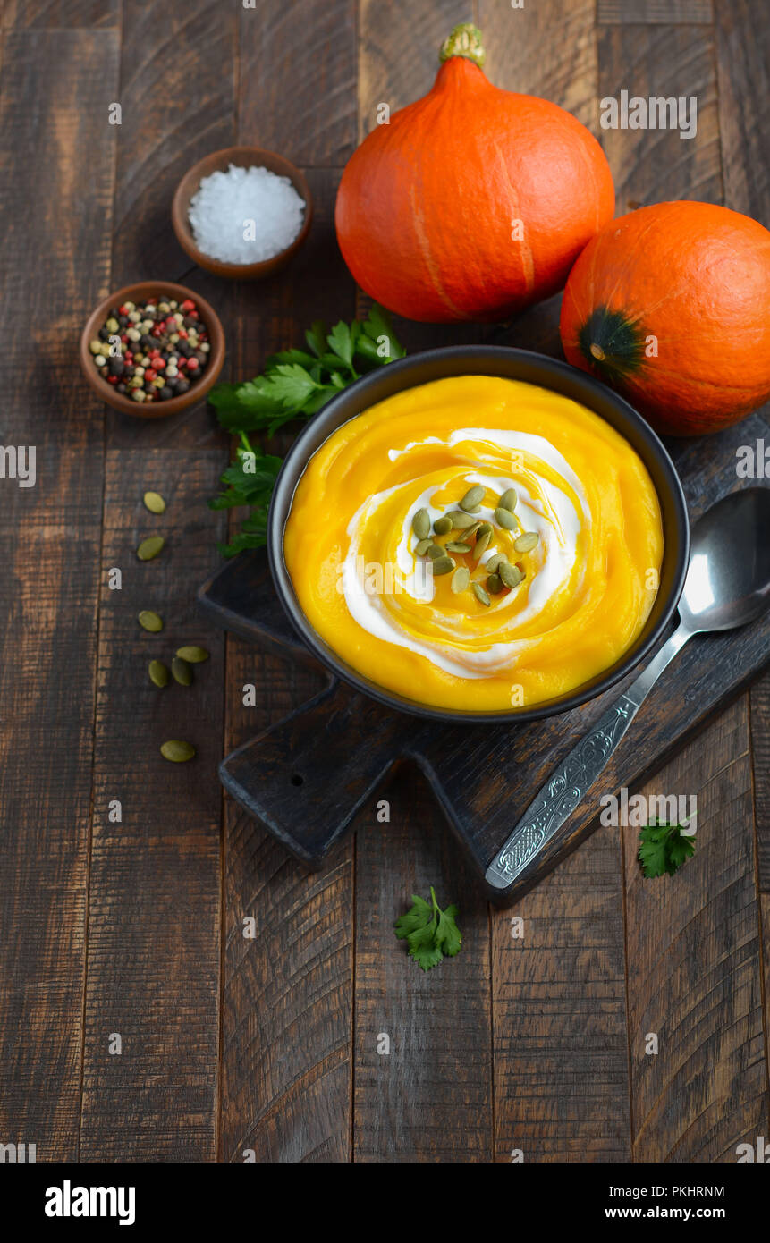 Pumpkin cream soup with cream and pumpkin seeds on rustic wooden table. Stock Photo
