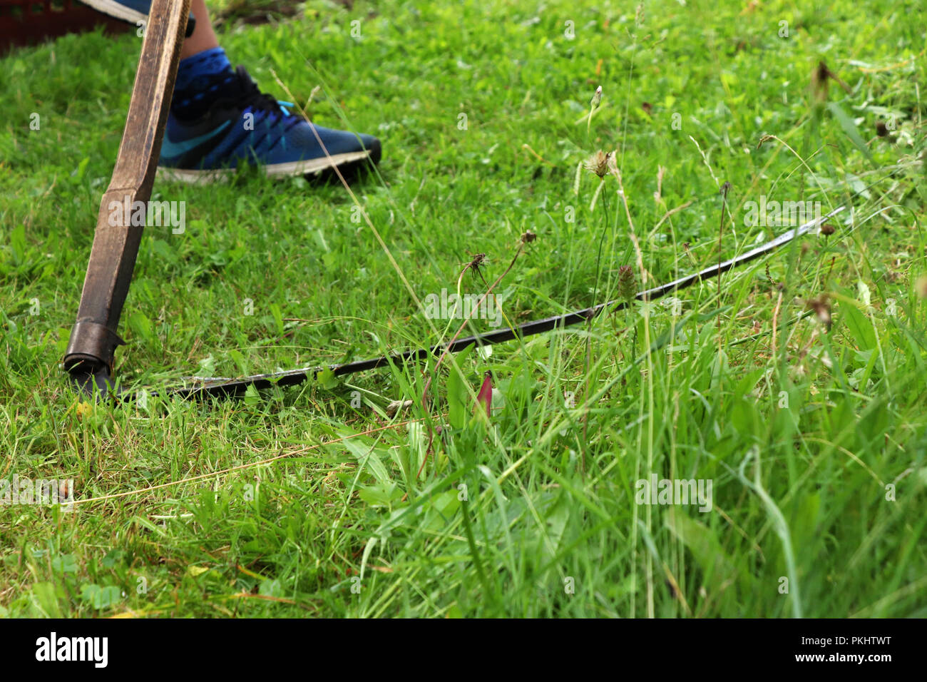 A man mowing a grass with old useful tool known as scythe.  In the village Stock Photo