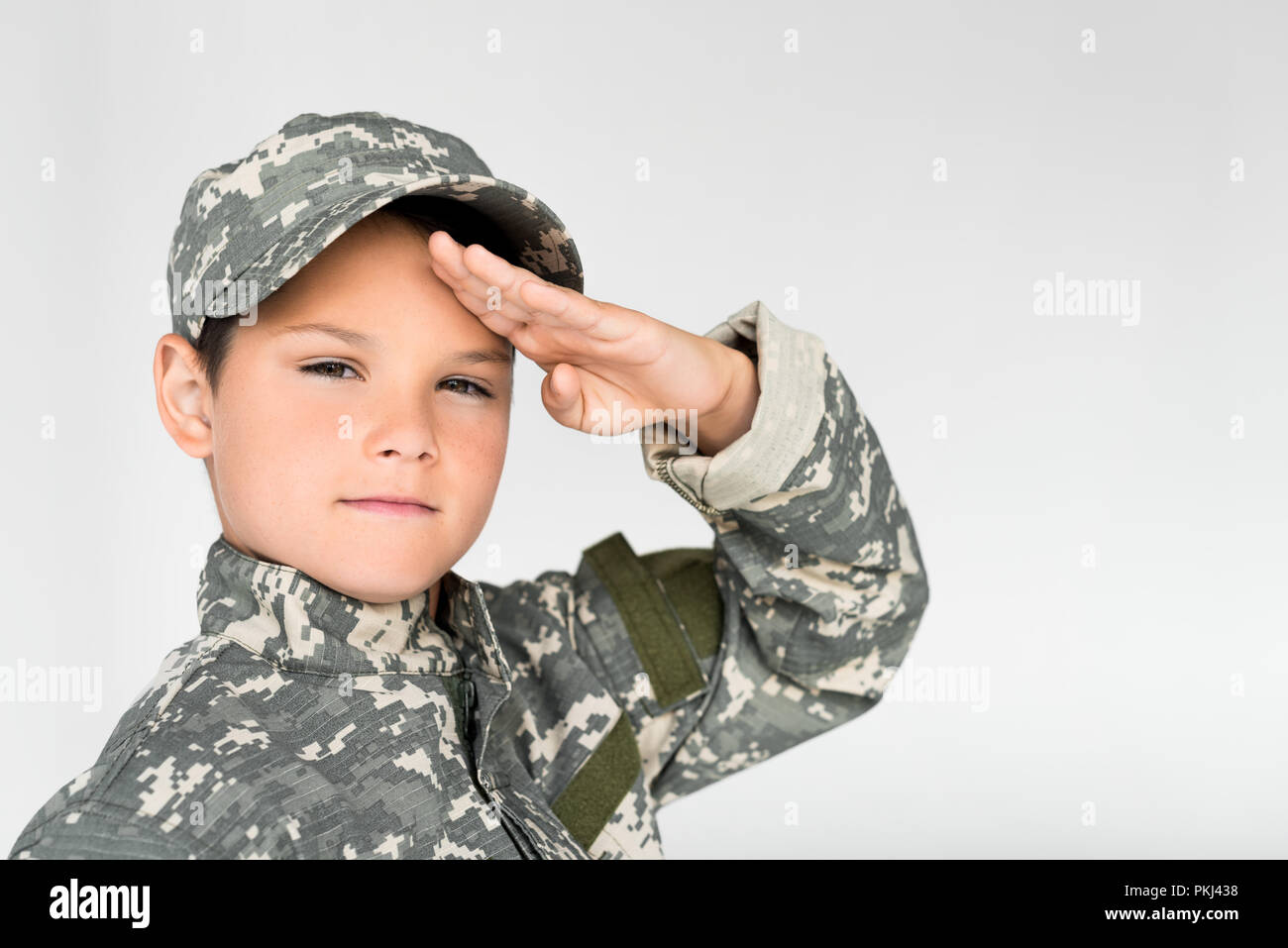 portrait of little kid in military uniform saluting on grey background