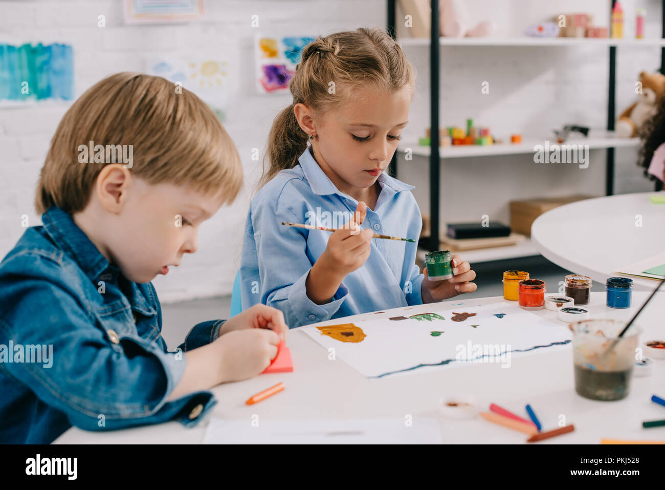 focused preschoolers drawing pictures with paints and paint brushes at