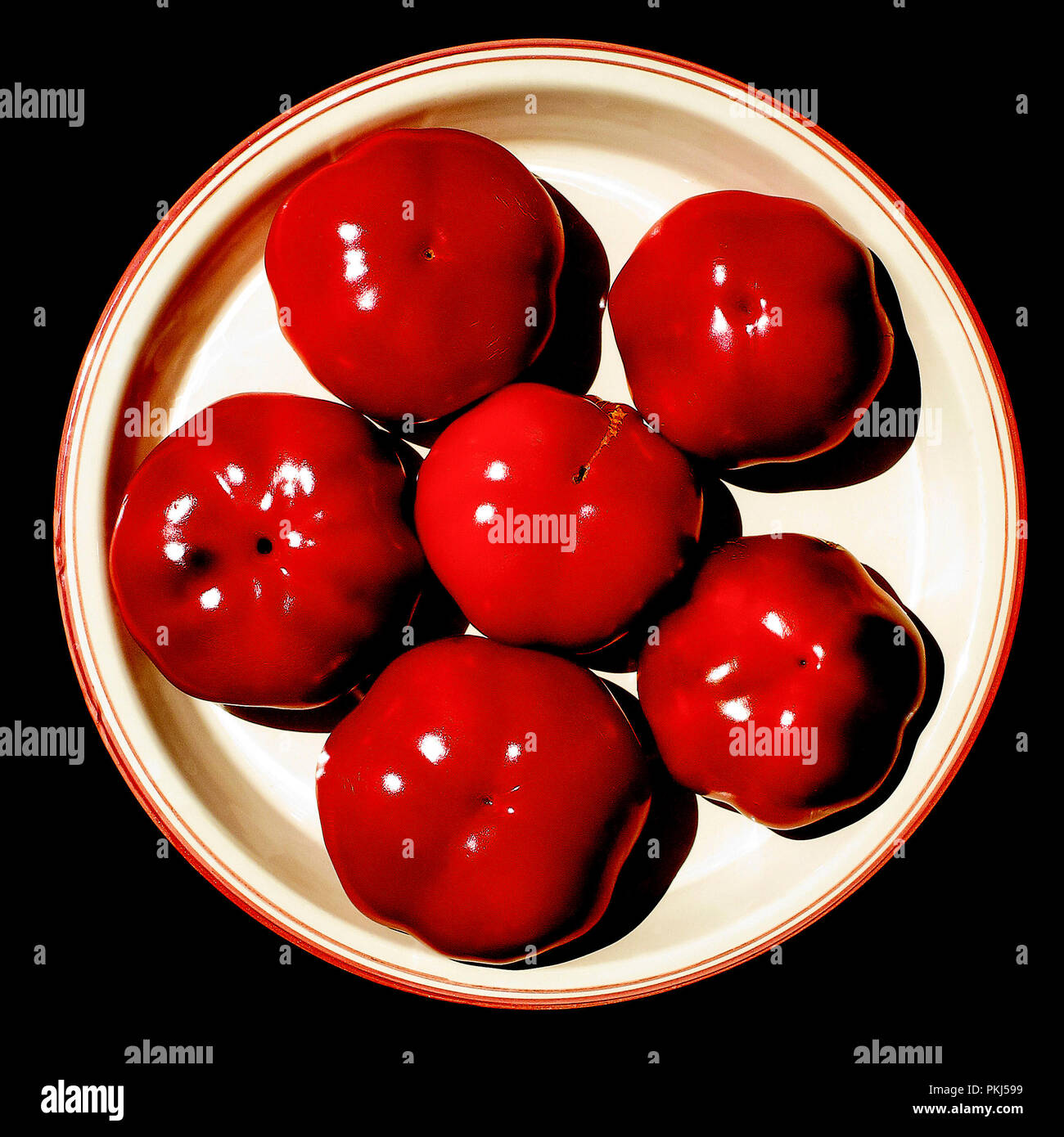 Still life photo: high contrast of red peppers on white plate, with black background... the three colors of alchemy. Stock Photo