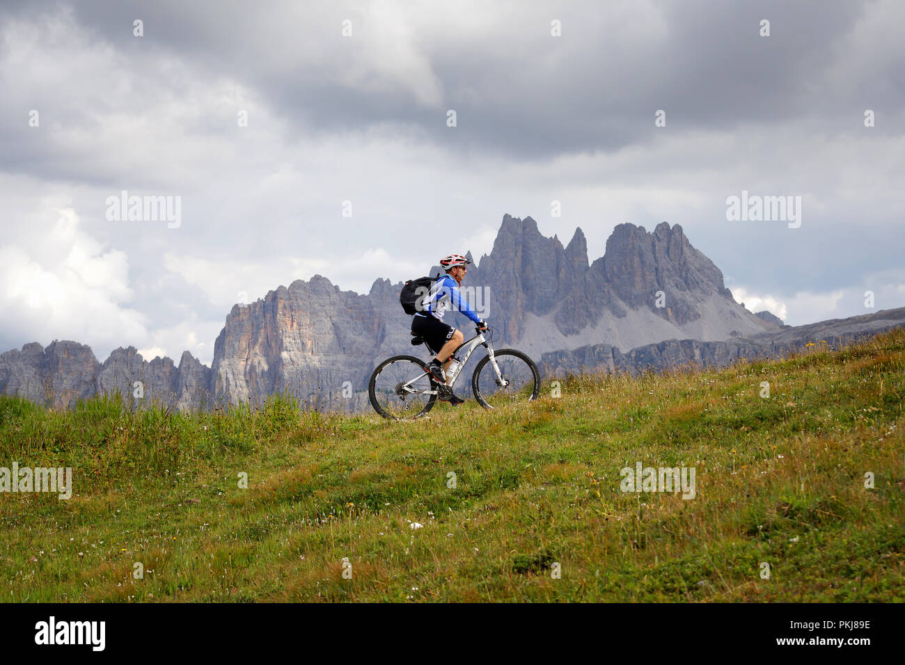 Cortina d'Ampezzo, Italy - August 18, 2018: a solo cyclist pedal uphill on  the mountain path, on a cloudy summer day. In the background, the peaks of  Stock Photo - Alamy
