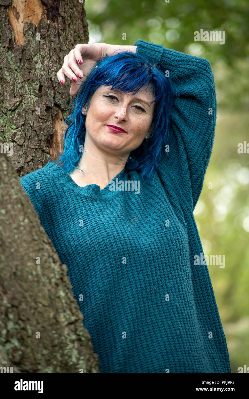 A Blue Haired Woman Wearing A Blue Jumper Leans Against A Tree Along A Forest Path Stock Photo Alamy