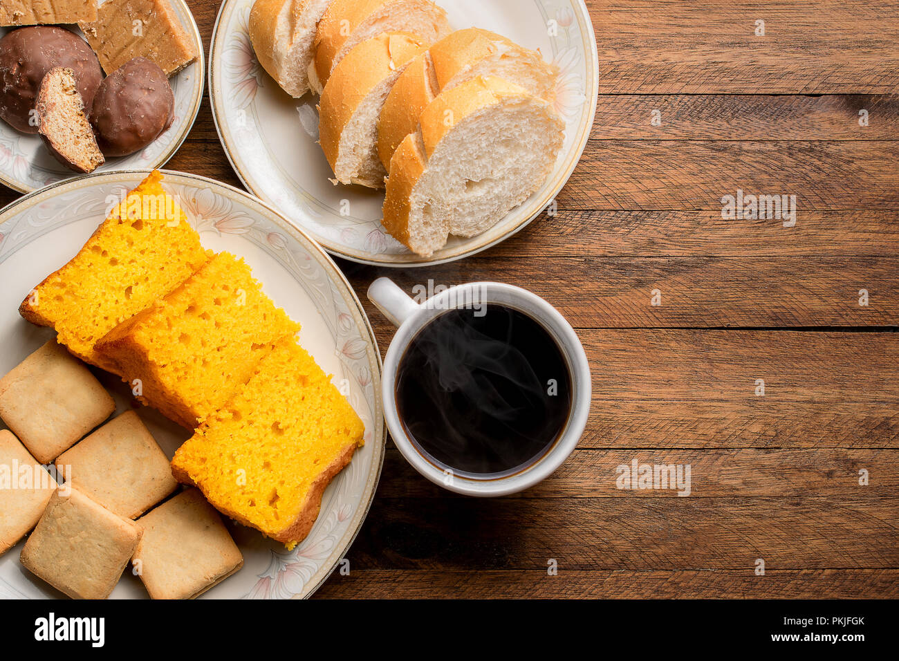 Breakfast food on a wooden table, carrot cake, bread, cookies and a hot coffee with steam coming out Stock Photo