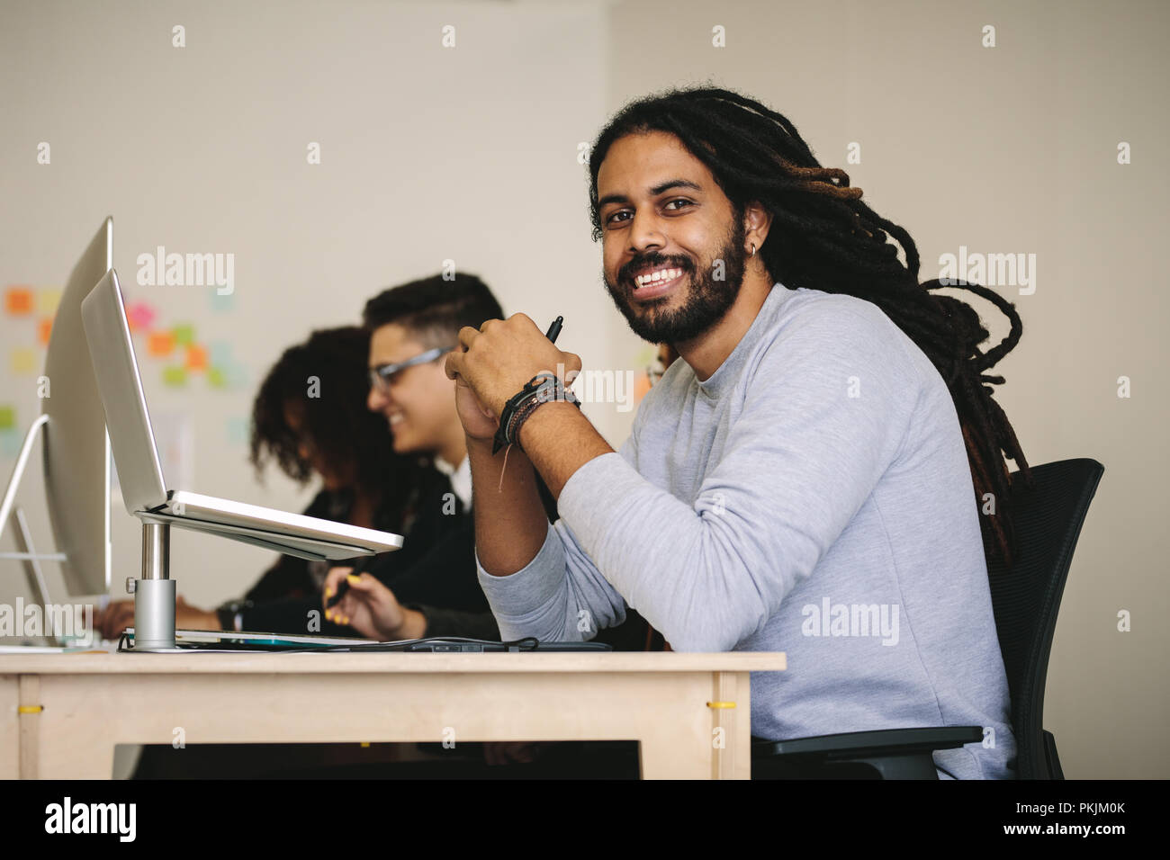 Smiling entrepreneur sitting at his desk with a laptop. Business people working in office sitting at their desks. Stock Photo