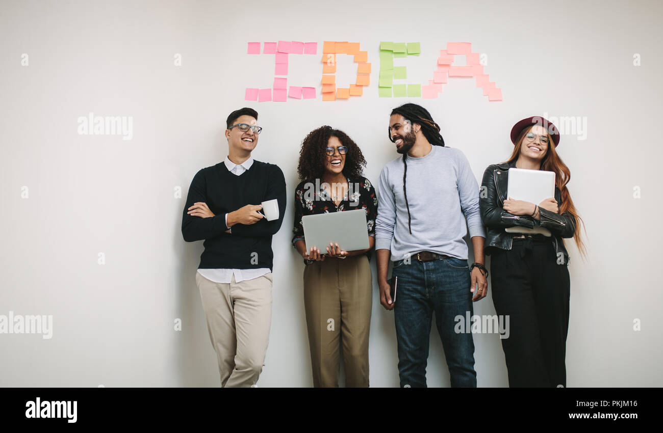 Cheerful business colleagues standing in office against a wall with the word idea written with sticky notes. business colleagues in cheerful mood rela Stock Photo