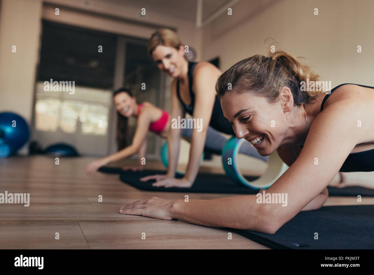 Women resting their abdomen on yoga or pilates wheel at the gym. Happy women doing pilates workout at the gym. Stock Photo