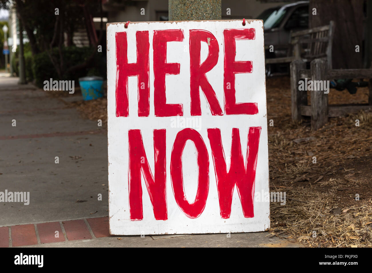 Here Now, painted sign with red letters on white background Stock Photo