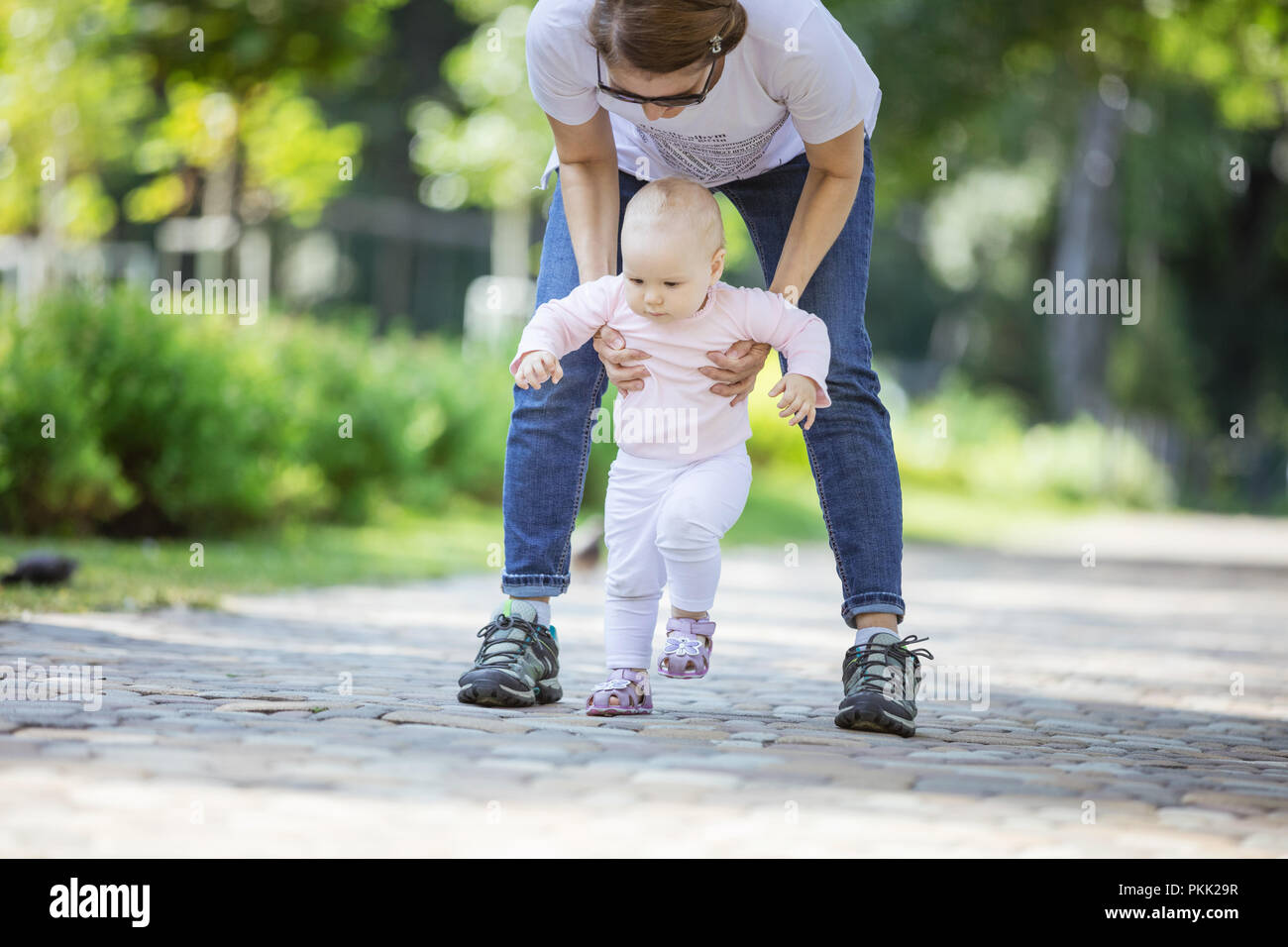 Mother supporting baby daughter and helping her make first steps. Mom ...