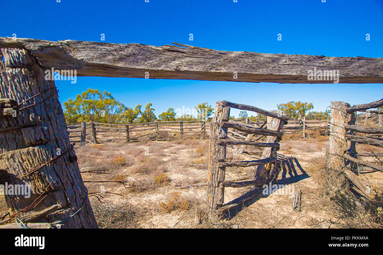 Arid Australian outback landscape with decaying old cattle yards on plains daubed with low vegetation under blue sky during drought in Queensland Stock Photo