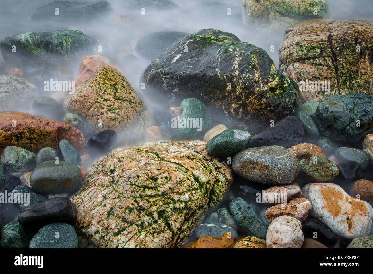 Rocks, stone, pebbles and blurred waves on the shoreline at Church Bay, Anglesey on the North Wales coast Stock Photo