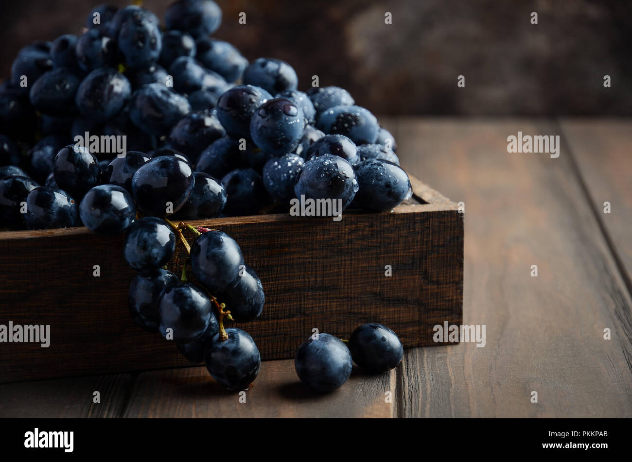 Fresh Black Grapes in Dark Wooden Tray on Wooden Table Selective focus Stock Photo