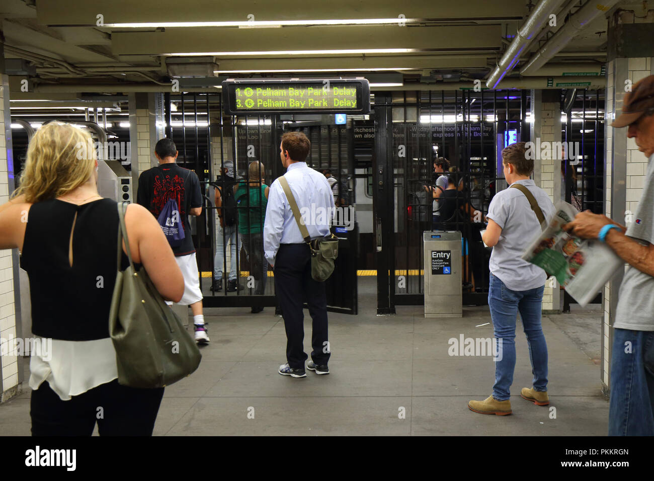 People standing outside a NYC Subway fare gate contemplating whether to enter the system while a departure board reflects major delays in the system. Stock Photo