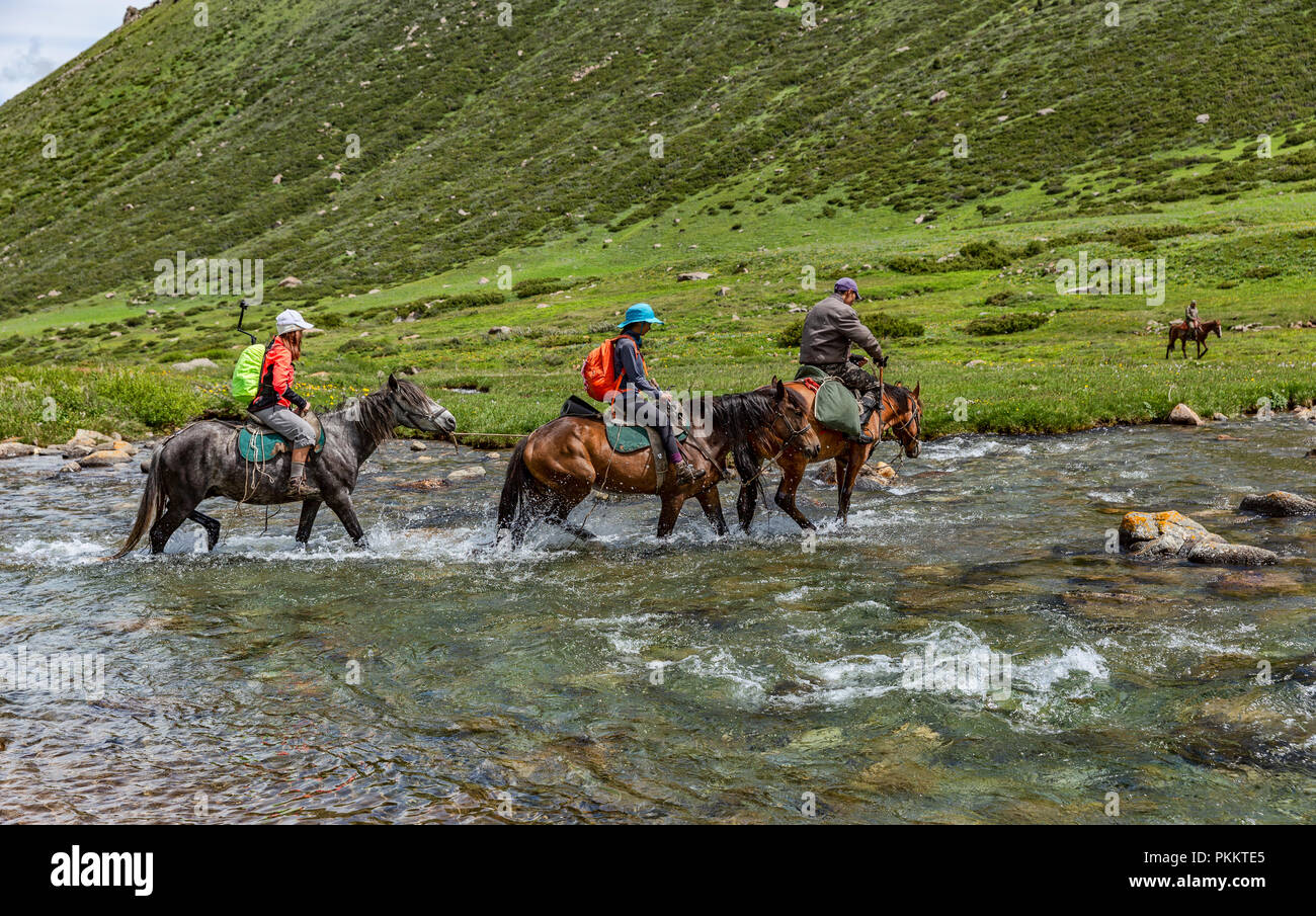 Trekkers ride horses across Tup River, Keskenkyia Loop trek, Jyrgalan, Kyrgyzstan Stock Photo