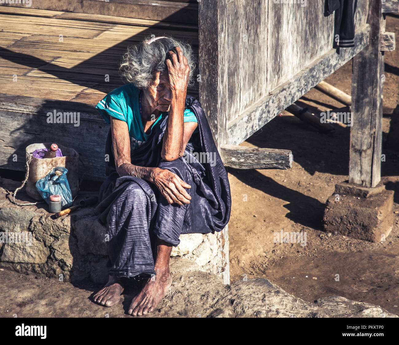 Elderly woman from the 1200 year-old Bena village near Bajawa town, on the island of Flores, shields her face from the biting sun. Stock Photo
