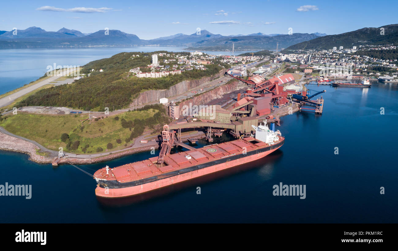 Aerial shot of a cargo ship anchoring in  port terminal and loading iron ore, Narvik, Norway Stock Photo