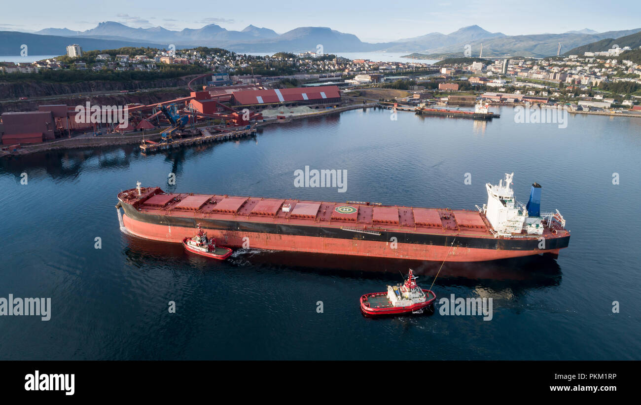 Aerial shot of a cargo ship approaching port terminal with help of towing ship, Narvik, Norway Stock Photo