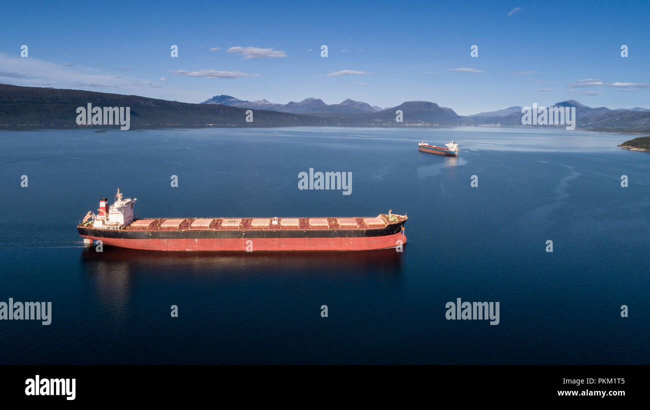 Aerial shot of a cargo ship on the open sea with other ship and mountains in the background, Narvik, Norway Stock Photo