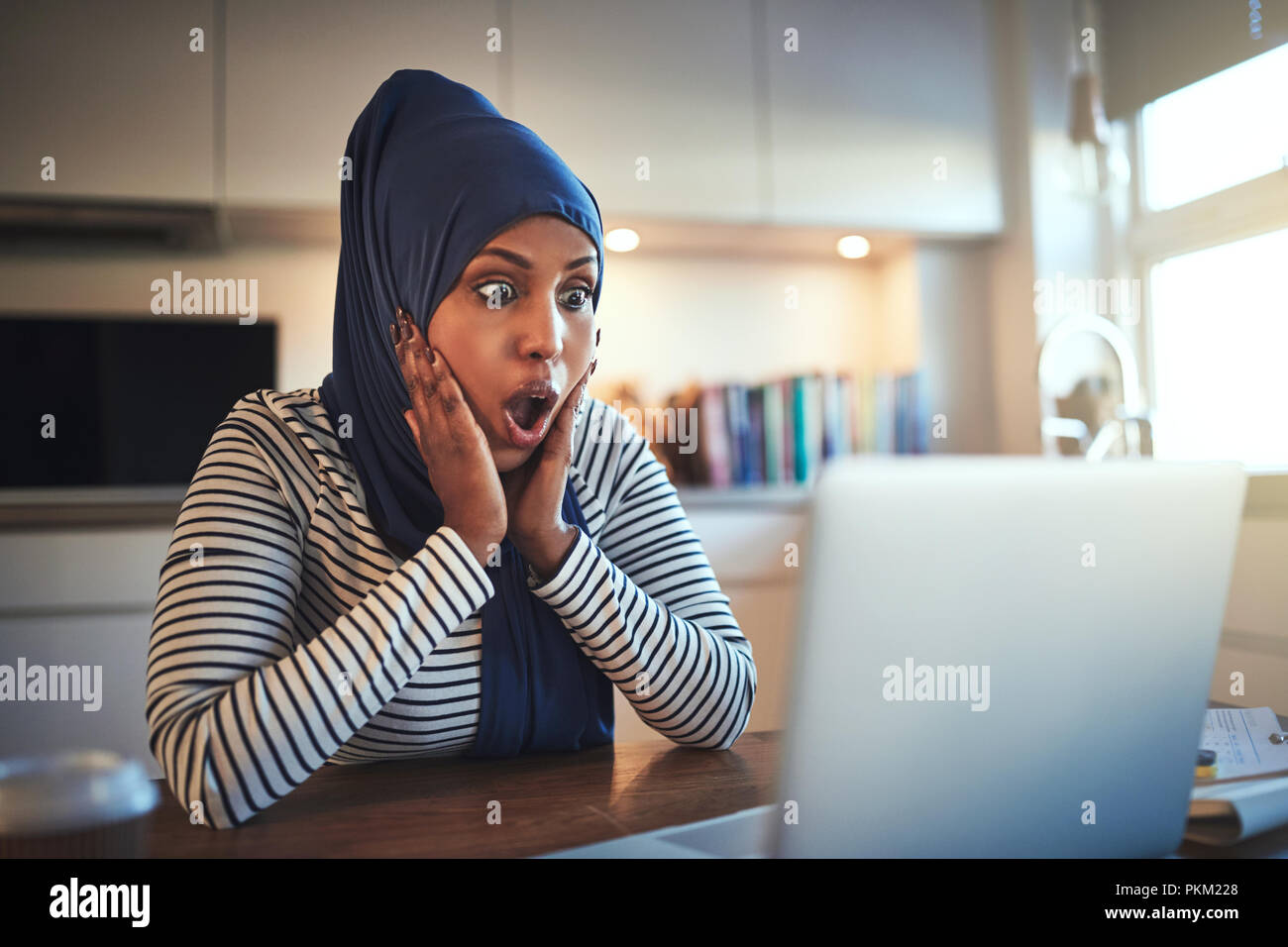 Young Arabic woman wearing a hijab looking shocked while working online ...